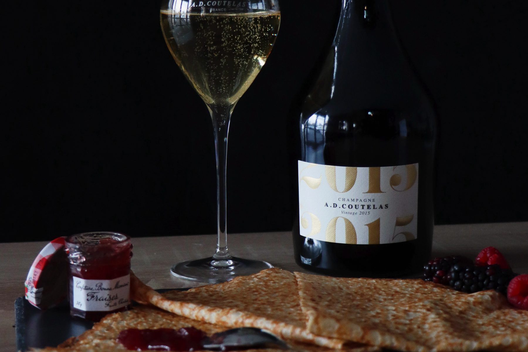 Gedeckter Moment: ein Glas Champagne A.D. Coutelas neben der Flasche, davor Crêpes mit Konfitüre und Beeren